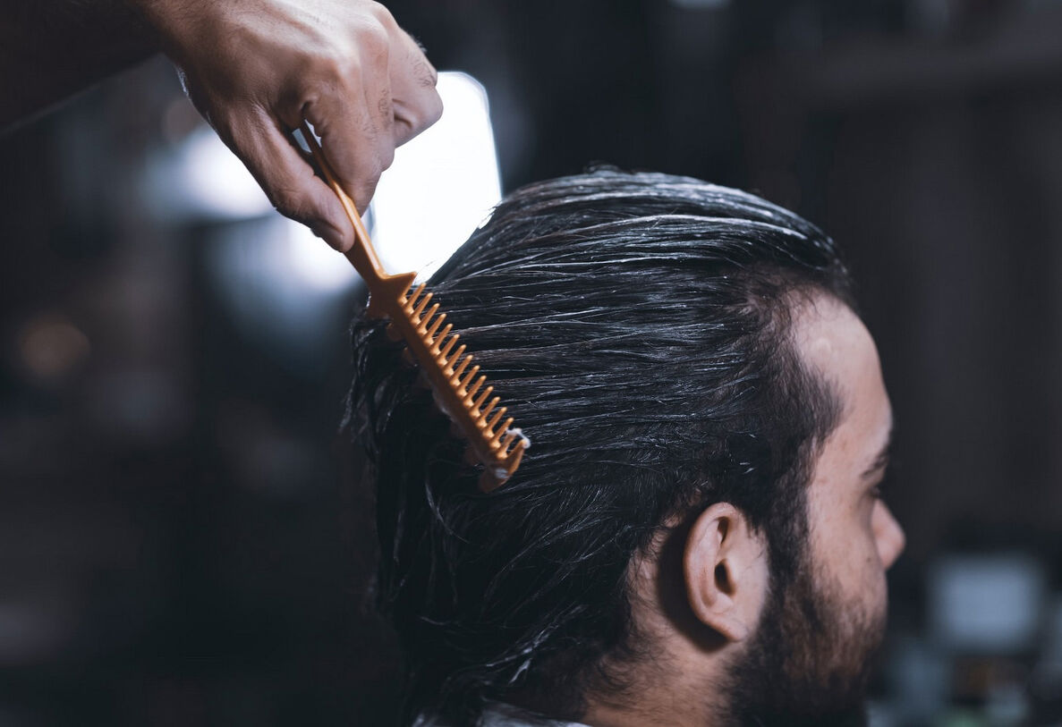 Person combing through wet, treated hair with a fine-toothed comb during a hair care routine.